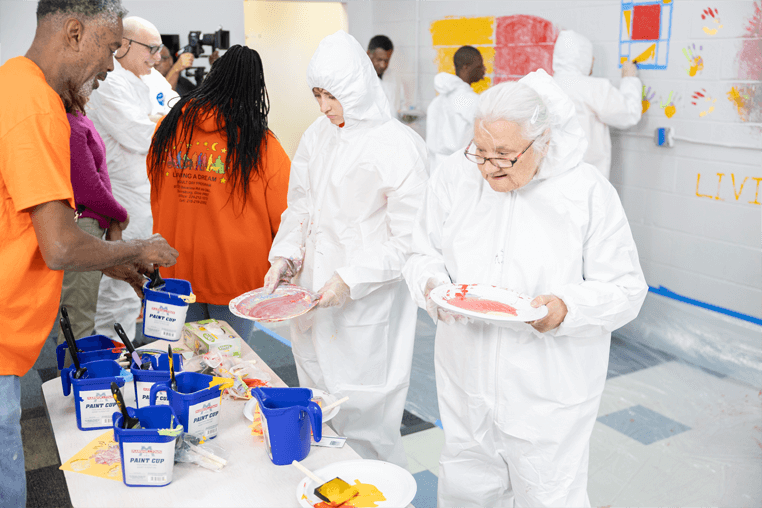 Two adults getting painting supplies ready to join others painting a wall